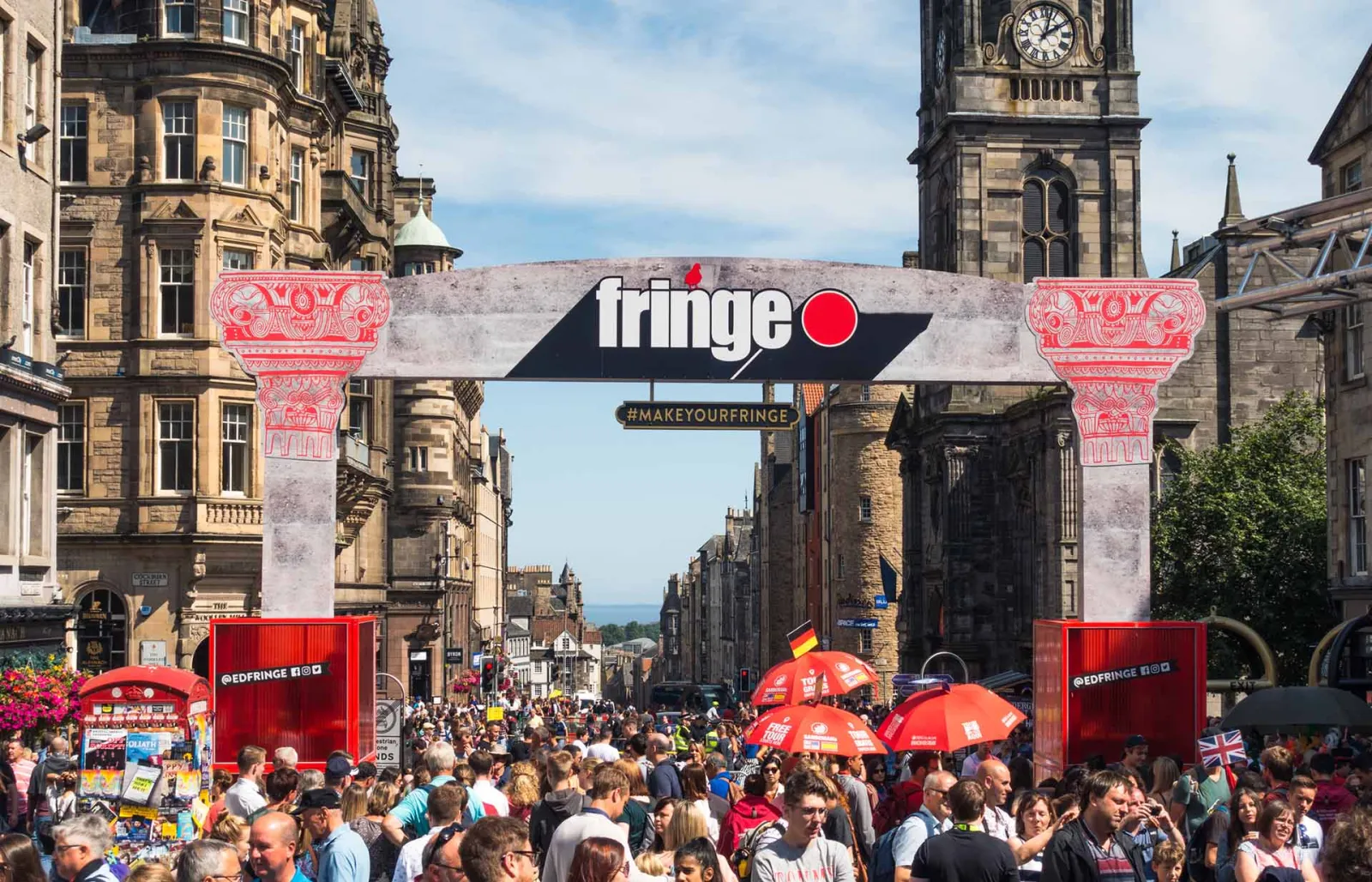 The Fringe arch over a crowded Royal Mile in Edinburgh, carrying the festival's logo and the EdFringe handle, at a previous edition